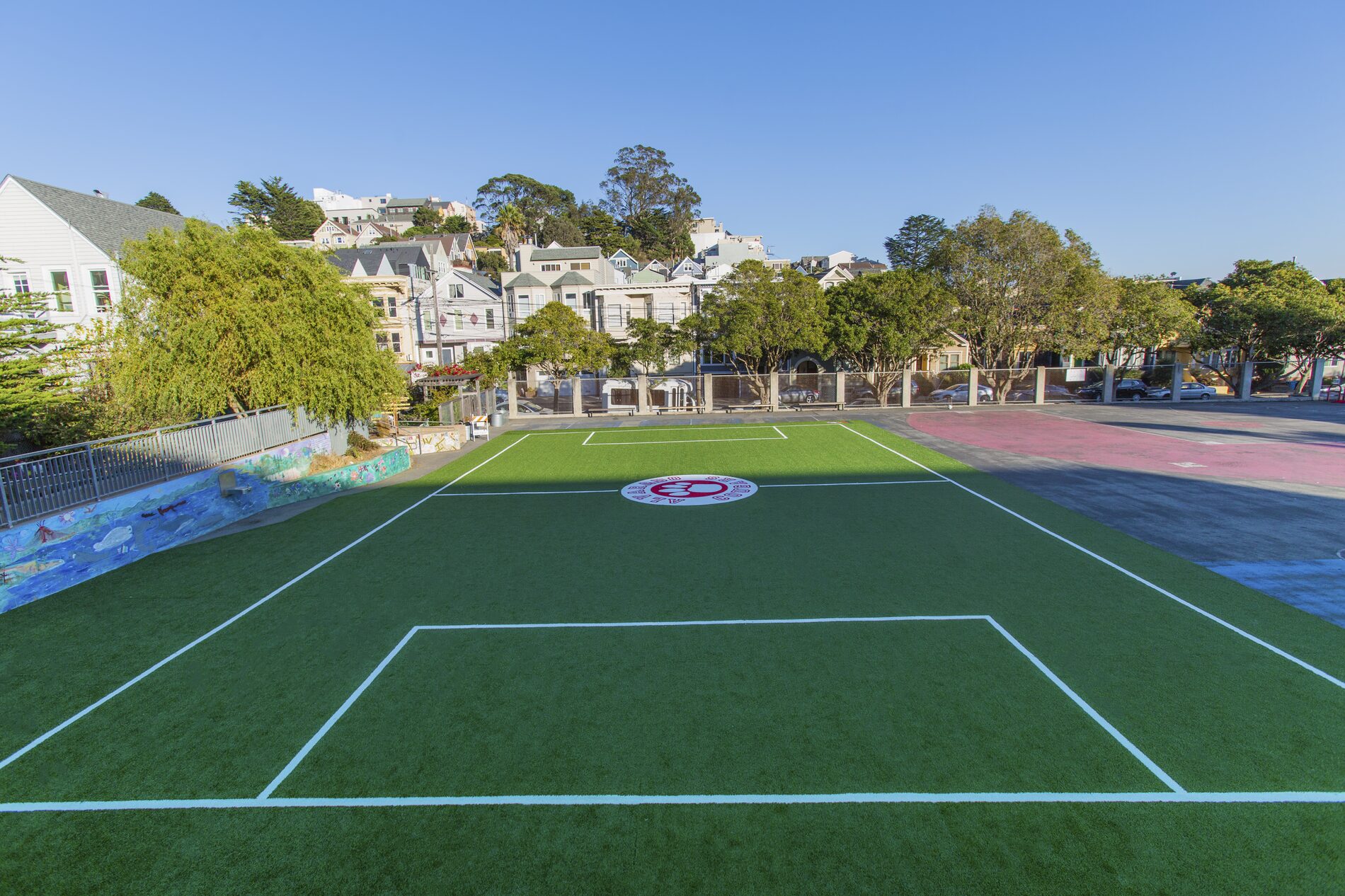 A custom soccer field built over a San Francisco schoolyard, with lines and a center logo, surrounded by the neighborhood